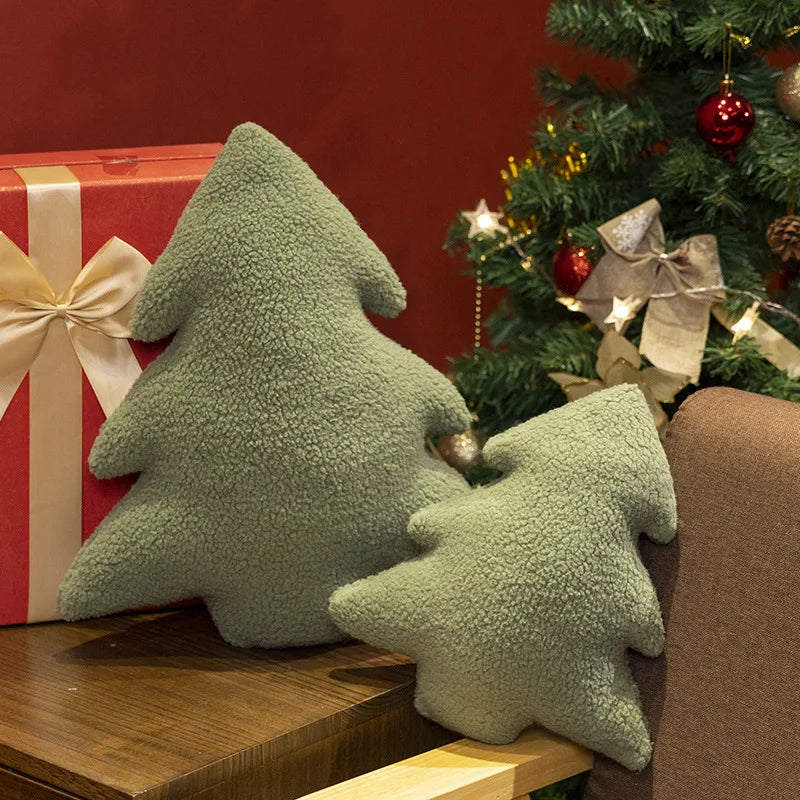 Green tree-shaped cushions on a wooden surface with a decorated Christmas tree in the background.
