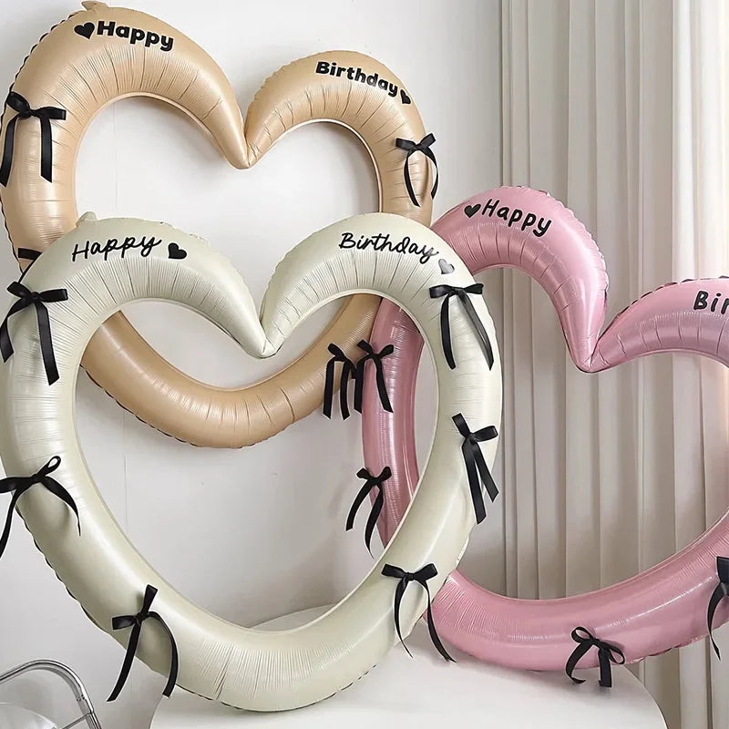 Heart-shaped balloons with 'Happy Birthday' text and black ribbons on a white background