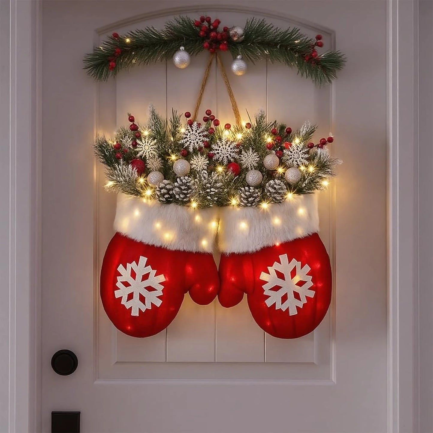 Decorative Christmas door hanger with red mittens, snowflakes, and lights on a white door.