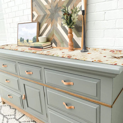 Gray dresser with bronze handles against a white brick wall