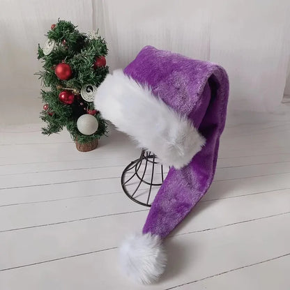Purple Santa hat with white fur trim on a wooden floor with a small decorated Christmas tree in the background.