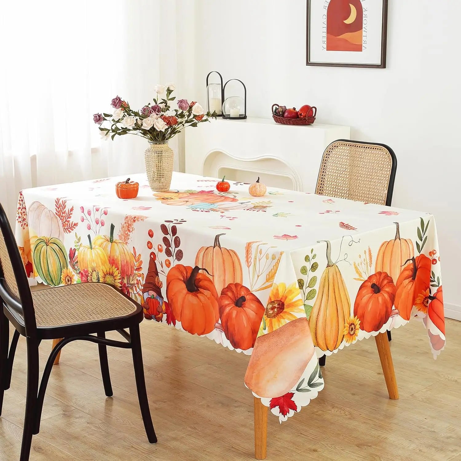 Table with a decorative tablecloth featuring pumpkins and autumn leaves, surrounded by chairs.