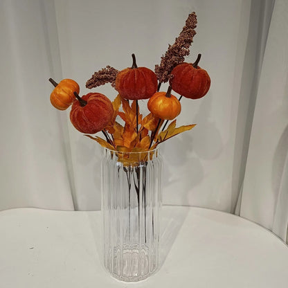 Decorative arrangement of pumpkins and leaves in a clear vase on a white surface.