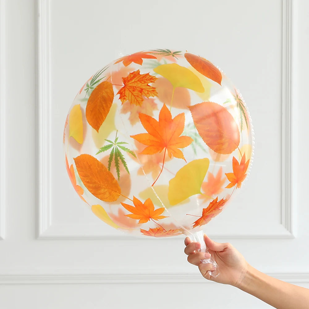 Clear balloon with autumn leaf pattern held by a hand against a white background