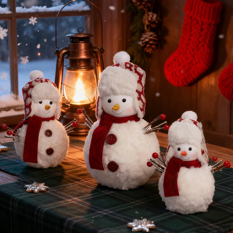 Three snowman figurines with red scarves and hats on a table with a lantern and Christmas stocking in the background.
