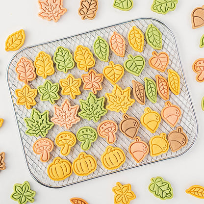 Assorted fall-themed cookies on a cooling rack with colorful leaves and pumpkins.