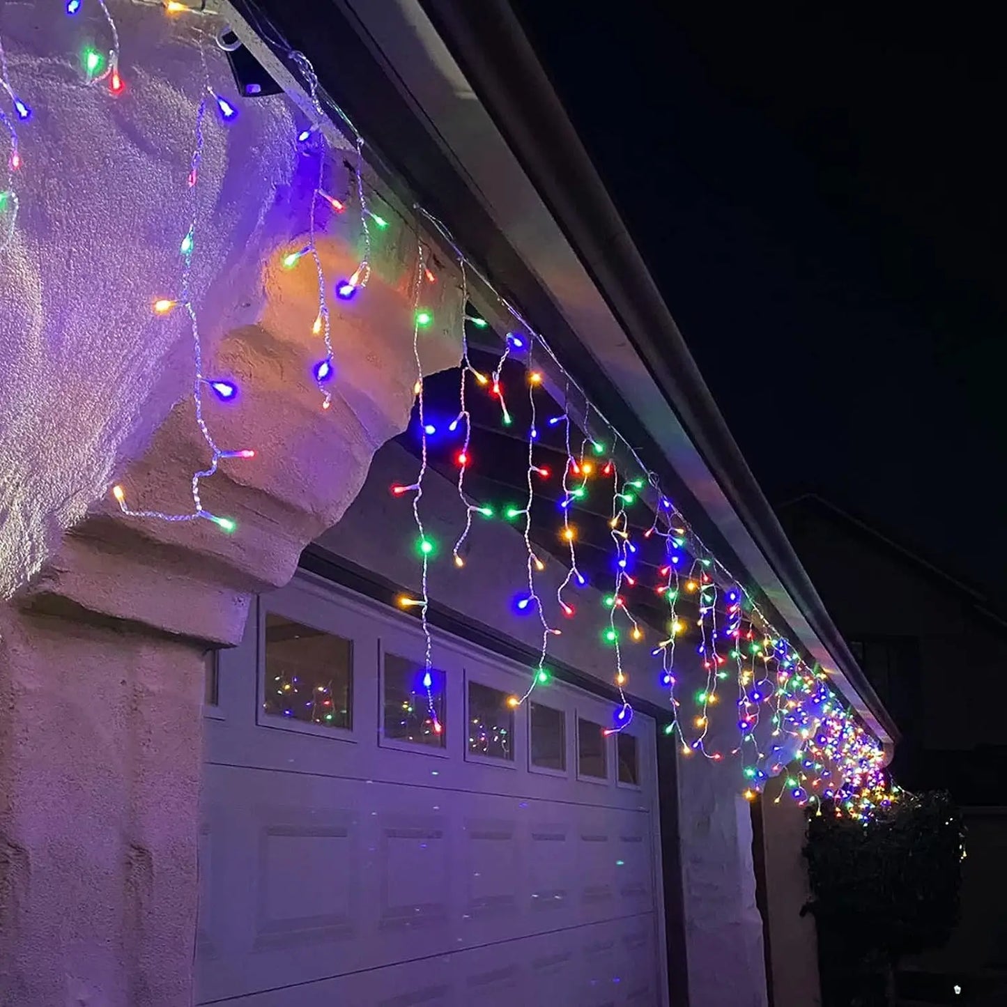 Colorful string lights draped over a garage roof at night.