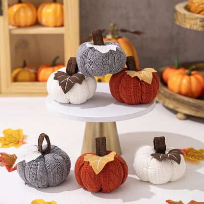 Knitted pumpkins in various colors on a white stand with pumpkins in the background.