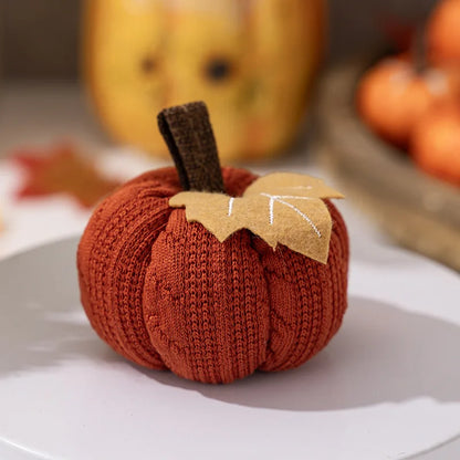 Knitted pumpkin decoration on a white plate with pumpkins in the background