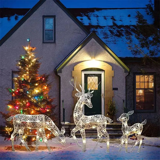 Decorative LED deer figures in front of a house with a Christmas tree at night.