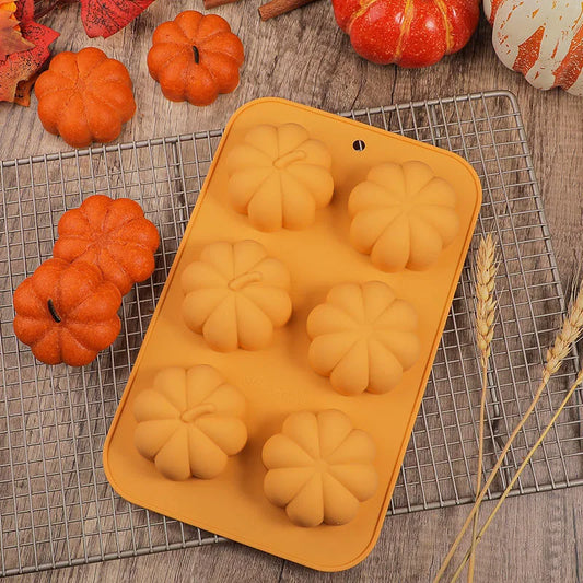Silicone mold shaped like pumpkins on a cooling rack with small pumpkins and autumn leaves around.
