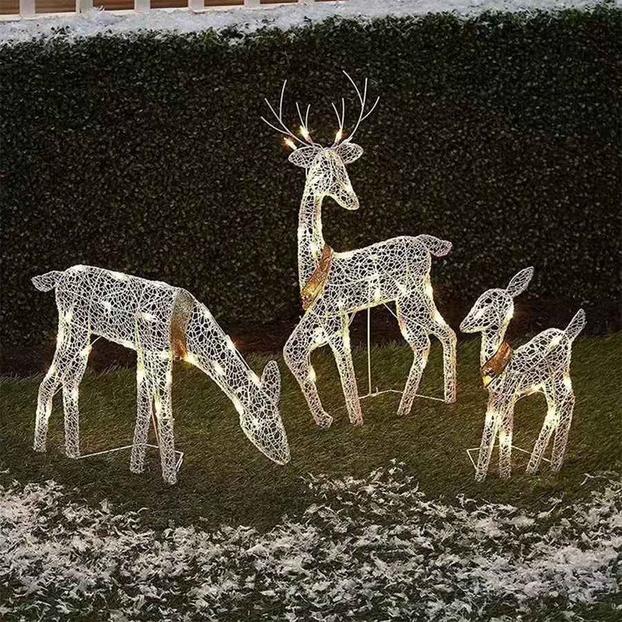 Set of three illuminated deer figures on a grassy area with a dark background