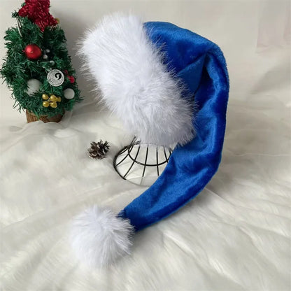 Blue Santa hat with white fur on a fluffy white surface with a small Christmas tree in the background.