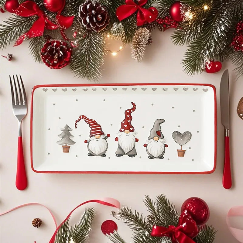 Decorative plate with cartoon gnomes, surrounded by Christmas decorations on a white table.