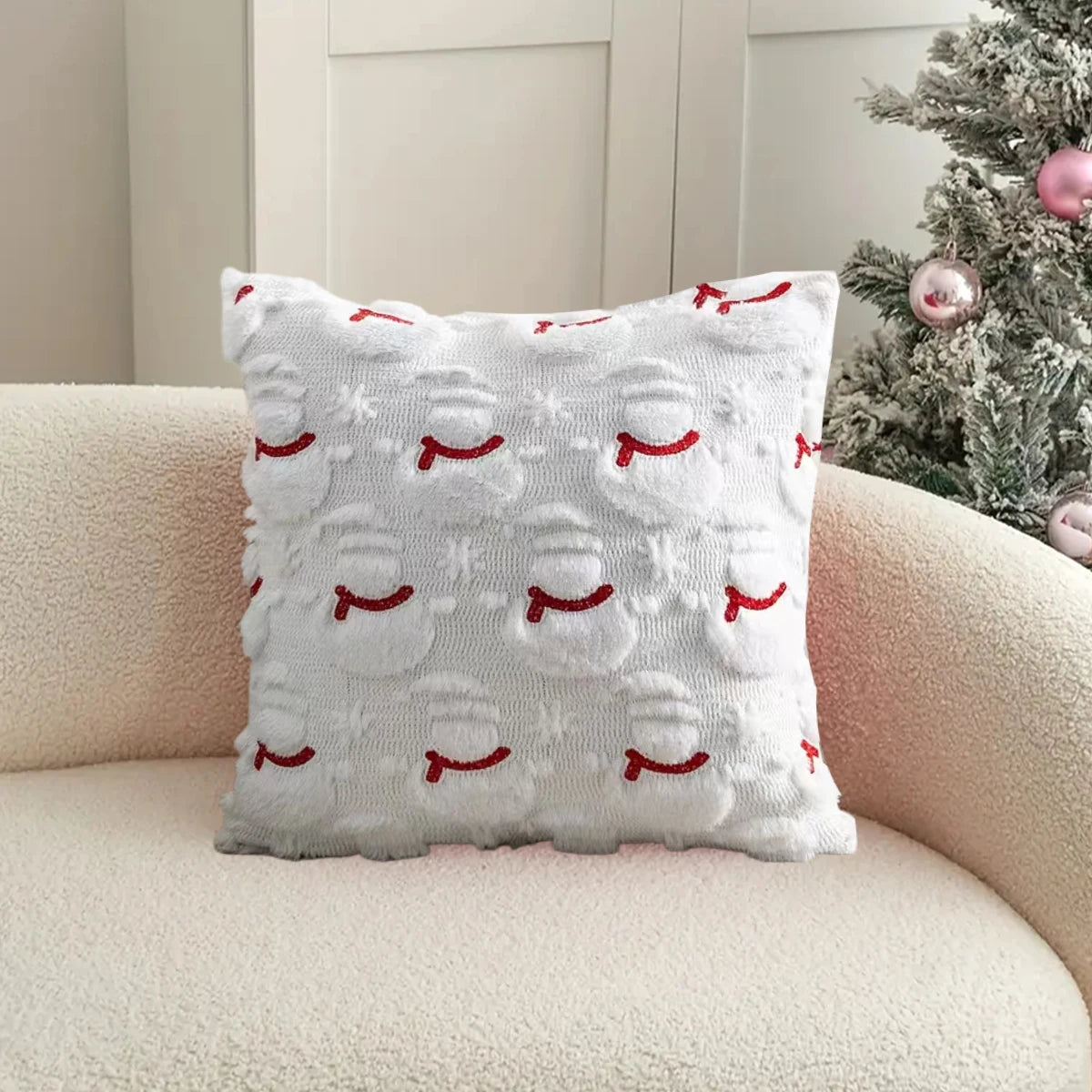 Decorative pillow with red snowman pattern on a beige couch next to a Christmas tree.