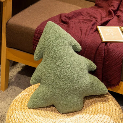 Green tree-shaped pillow on a woven ottoman with a red blanket and wooden chair in the background.