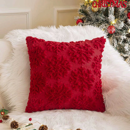 Red textured pillow on a white fur surface with a Christmas tree in the background