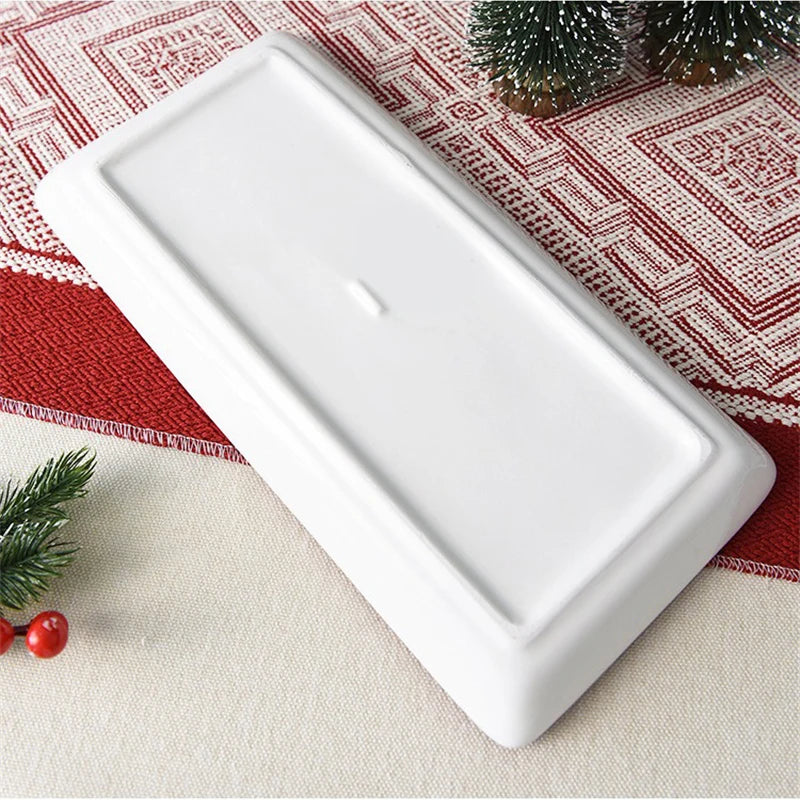 The underside of a white rectangular plate on a red and white checkered tablecloth with Christmas decorations.