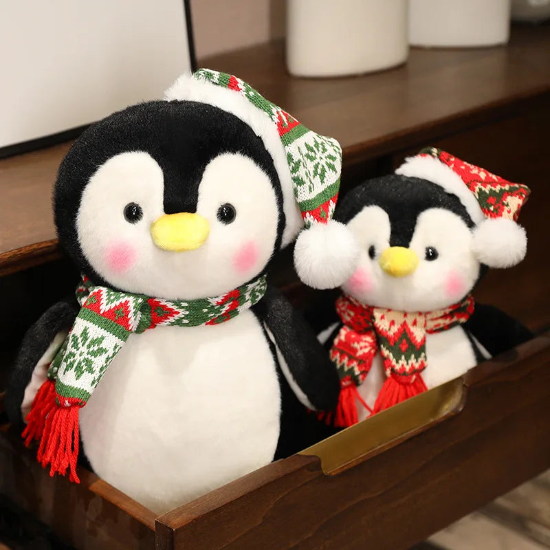 Two plush penguins wearing festive hats and scarves on a wooden surface.