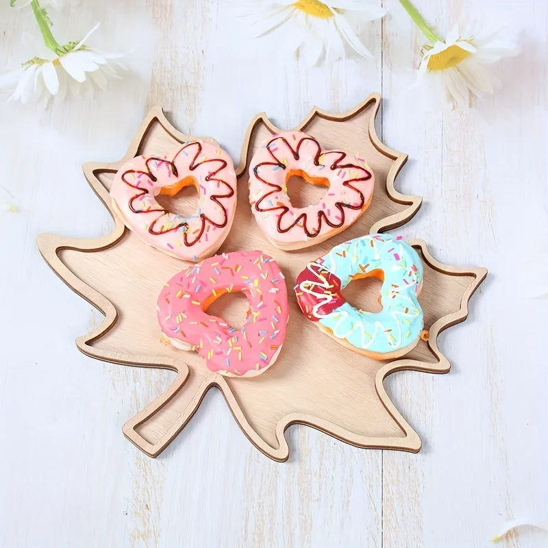 Wooden leaf-shaped cookie cutter with four donut-shaped cookies on a light wooden background.