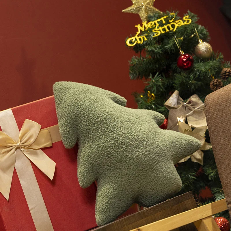 Green tree-shaped pillow on a red gift box with a Christmas tree in the background.