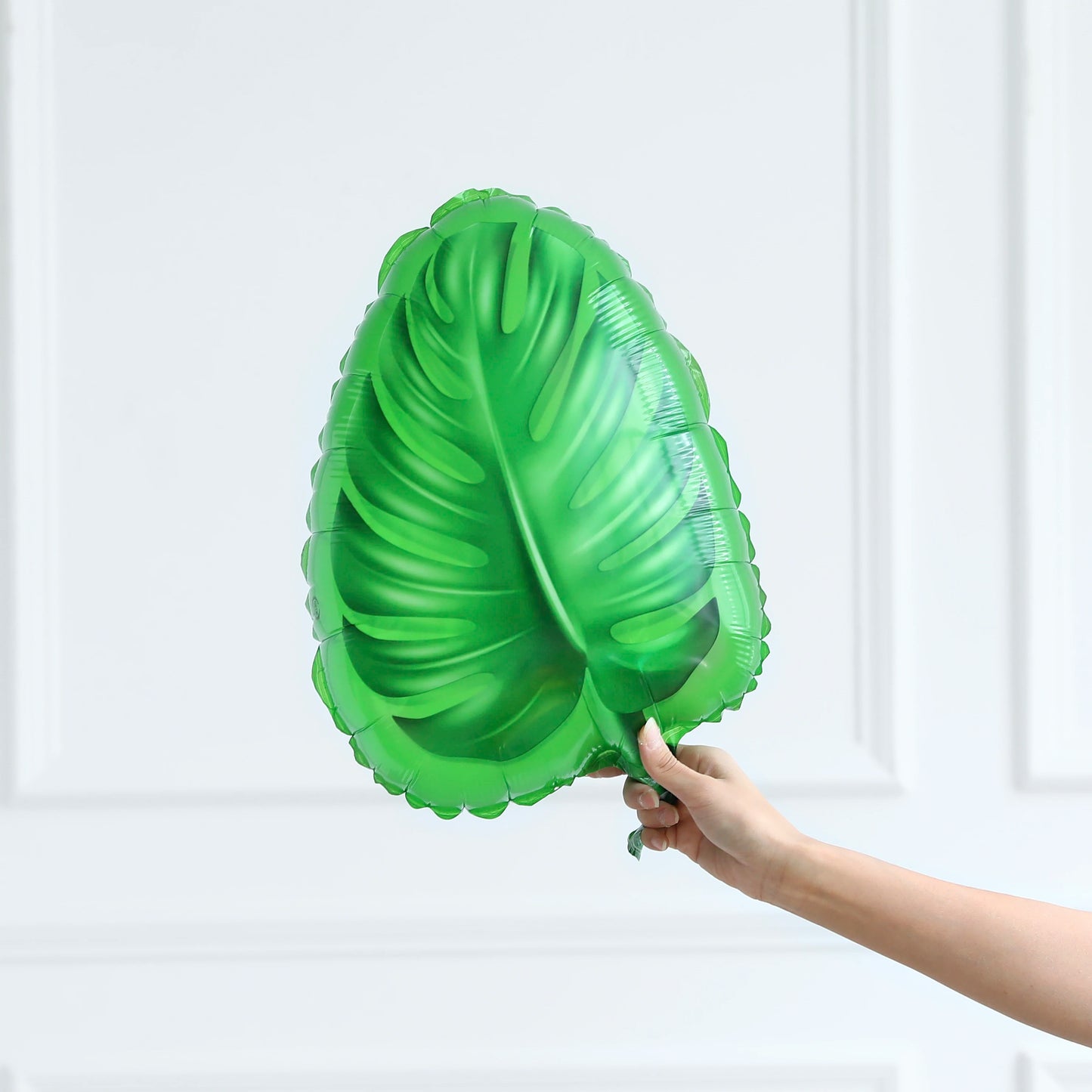 Hand holding a green leaf-shaped balloon against a white background