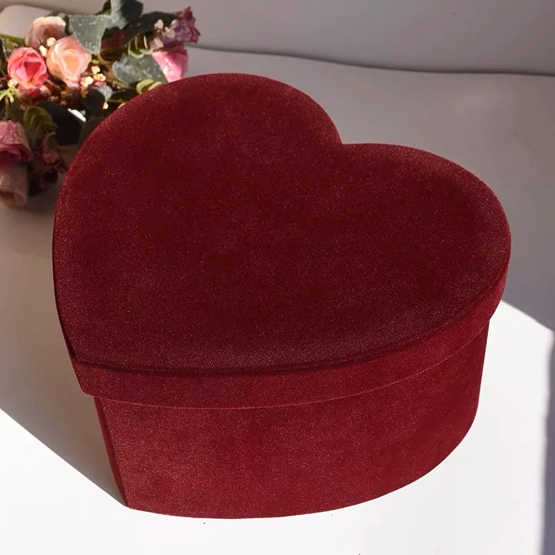 Heart-shaped red velvet box on a white surface with flowers in the background