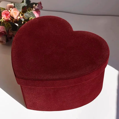 Heart-shaped red velvet box on a white surface with flowers in the background