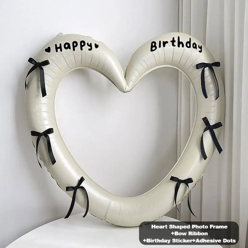 Heart-shaped photo frame with birthday stickers and ribbons on a white background