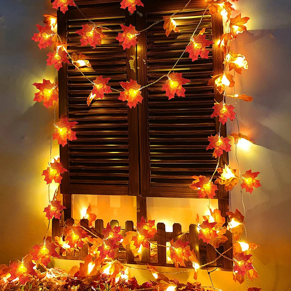 Decorative string lights shaped like autumn leaves in front of wooden shutters.