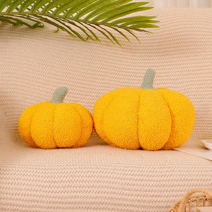 Two yellow pumpkin-shaped cushions on a beige textured surface with a green leaf in the background.