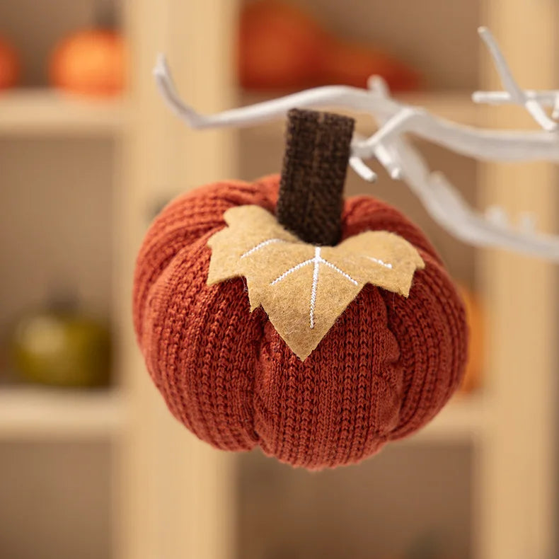 Knitted pumpkin decoration with a leaf on a branch against a blurred background
