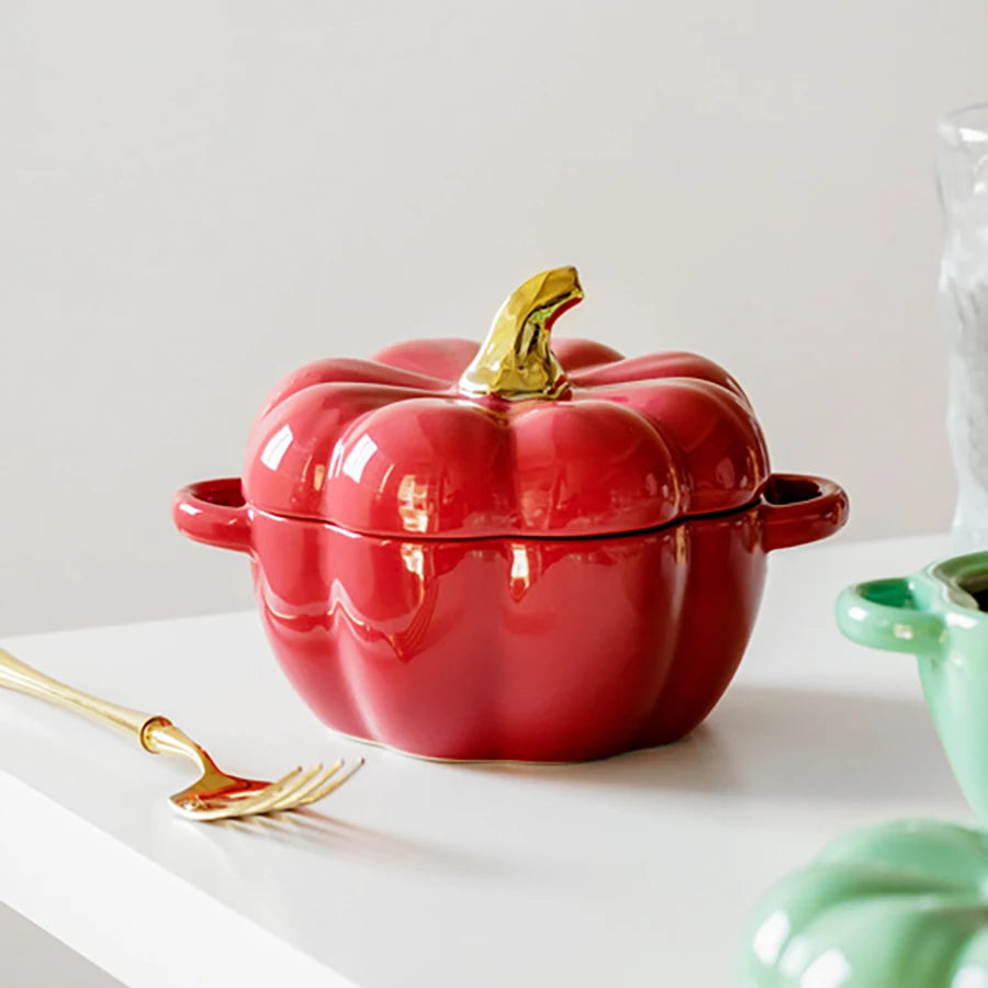 Red pumpkin-shaped cookware with a gold lid knob on a white surface.