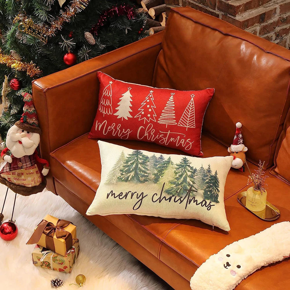 Decorative pillows with Christmas designs on a brown couch next to a Christmas tree.