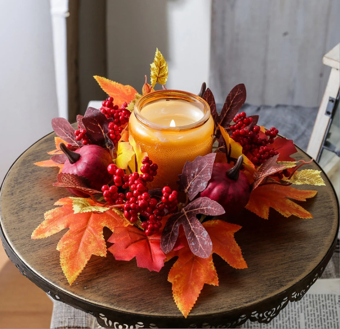 Decorative candle holder with autumn leaves and berries on a wooden table.