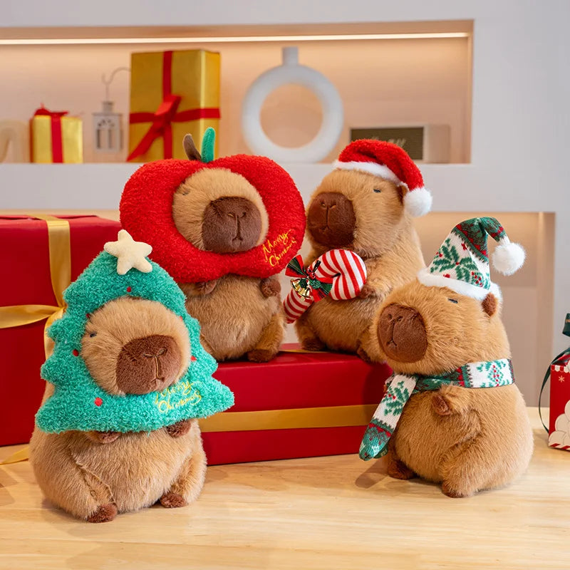 Four capybara plush toys wearing festive hats and scarves on a wooden surface with gift boxes in the background.