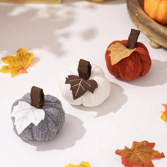 Knitted pumpkins in gray, white, and orange with leaf decorations on a light background.