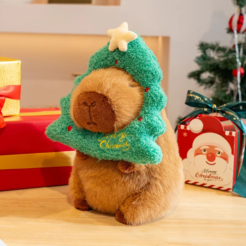 Plush capybara toy in a Christmas tree costume with presents and a Santa Claus box in the background.