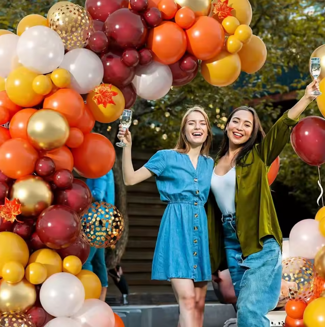 Two women celebrating with balloons and drinks outdoors.