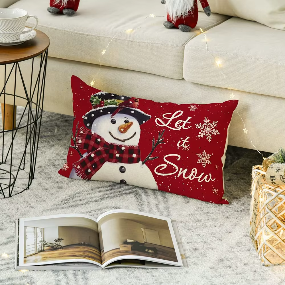 Red pillow with snowman design and 'Let it Snow' text on a living room floor.