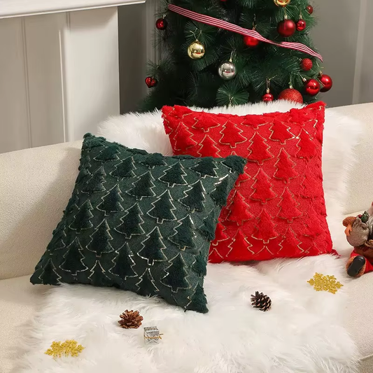 Two Christmas-themed pillows, one green and one red, on a white couch with a decorated Christmas tree in the background.