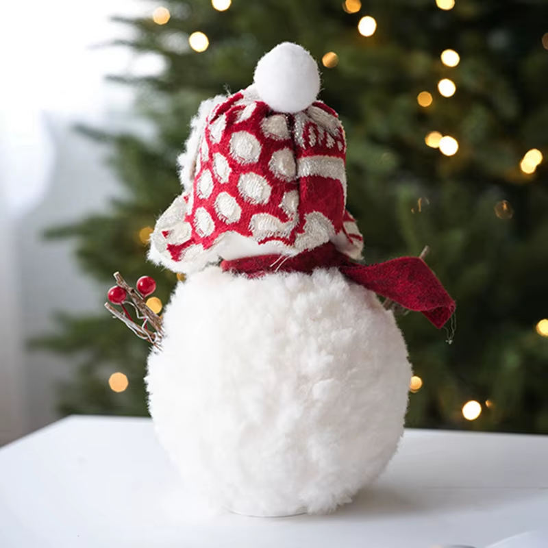 White snowman figurine with a red and white patterned hat and scarf, Christmas tree in the background.