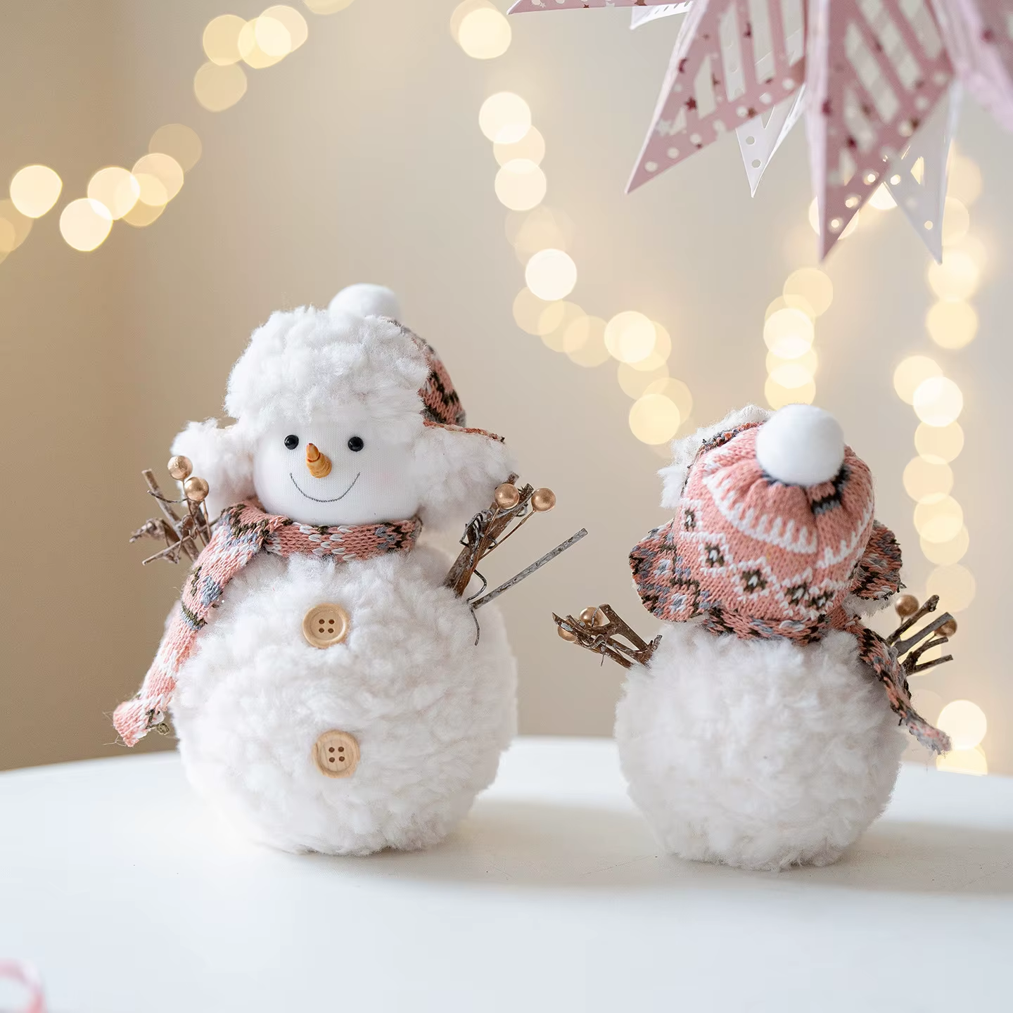 Two decorative snowmen with scarves and hats against a softly blurred background with lights.