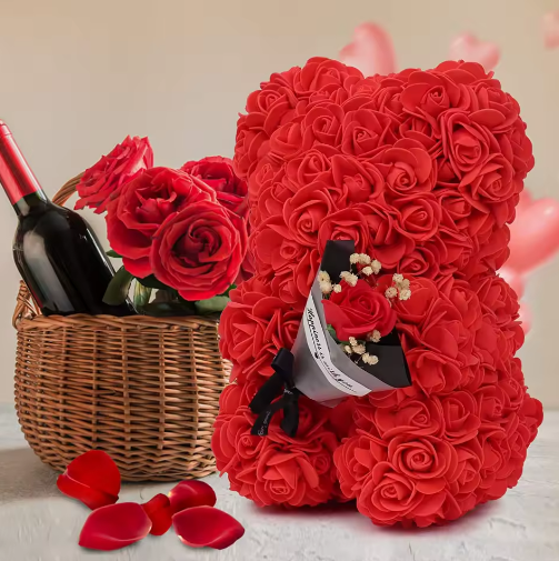 Red rose teddy bear holding a bottle of wine with a basket of roses in the background.